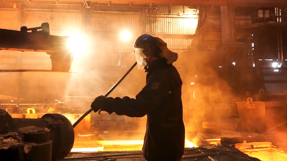 Side view of the perator remove waste from furnace pipe at the iron melting plant. Stock footage. Man worker in heat resistant suit cleaning high temperature furnace.